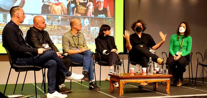 A panel of 5 people sit in a semi-circle in front of a large projection of images.