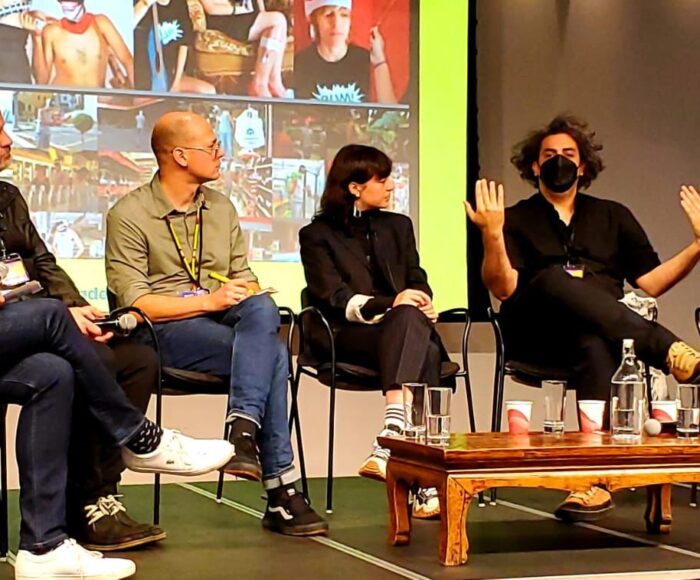 A panel of 5 people sit in a semi-circle in front of a large projection of images.