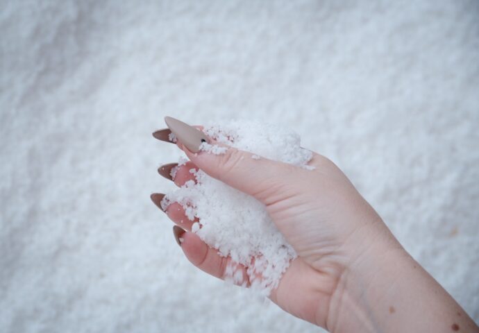 A hand with taupe stiletto nails holds a handful of salt.