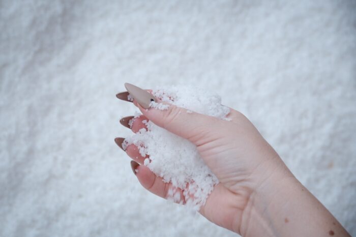 A hand with taupe stiletto nails holds a handful of salt.