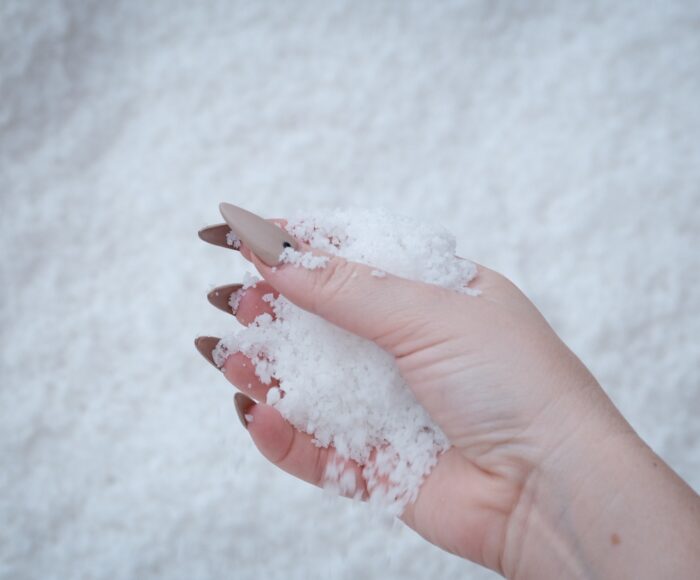 A hand with taupe stiletto nails holds a handful of salt.