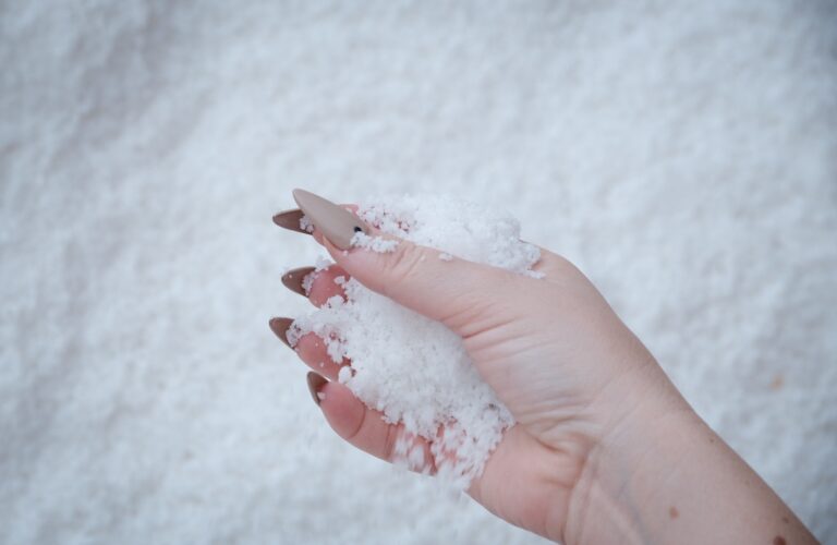 A hand with taupe stiletto nails holds a handful of salt.