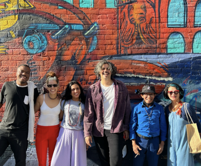 A group of six smiling people gathering for a picture in front of a big, colourful graffiti wall.